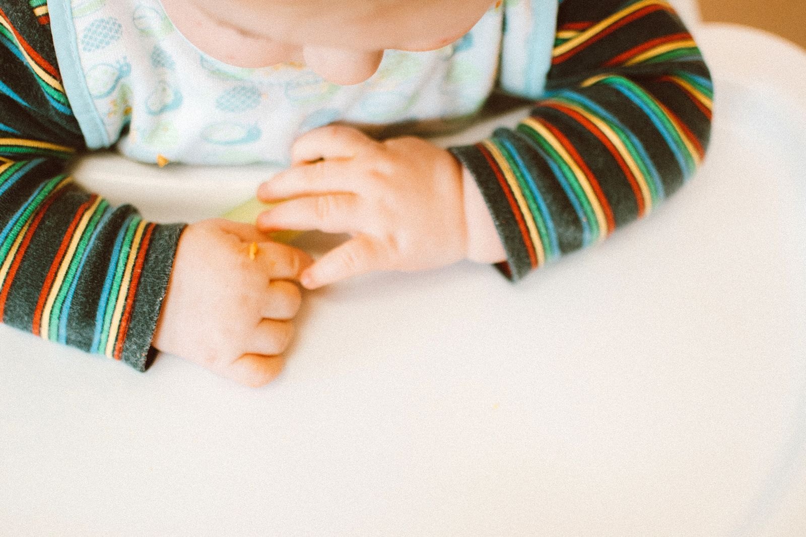 Close-up van de handjes van een baby in de kinderstoel die met duim en wijsvinger een stukje eten oppakt