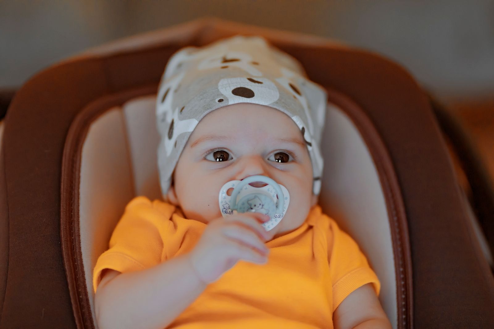 Baby in een babyschaal met een mutsje op, vastgehouden speentje