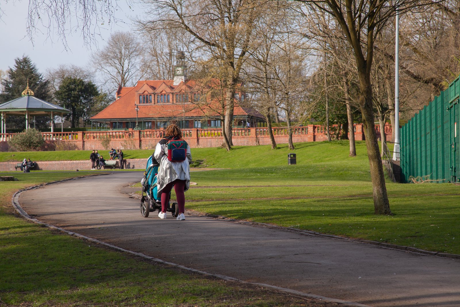 Een ouder duwt een moderne kinderwagen over een pad in een park met kale winterbomen