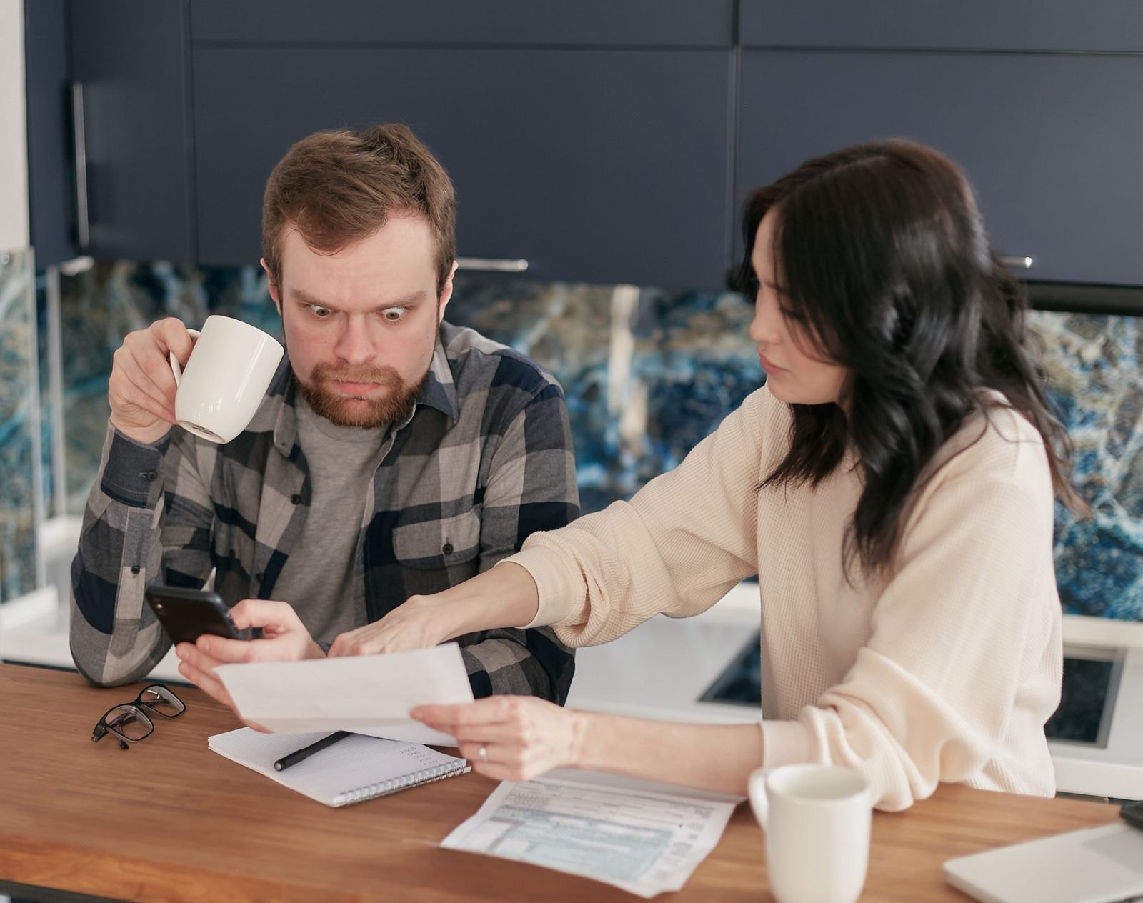 Een stel aan de keukentafel dat samen een envelop met een rekening bekijkt, met zichtbare spanning tussen hen