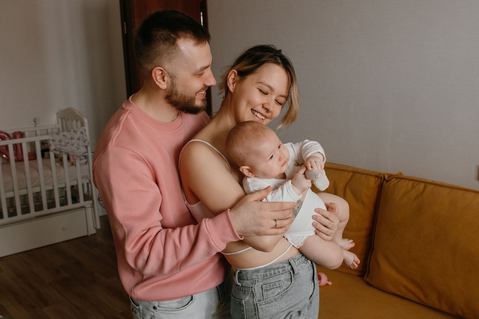 Een jong ouderpaar houdt samen glimlachend hun baby vast in de babykamer