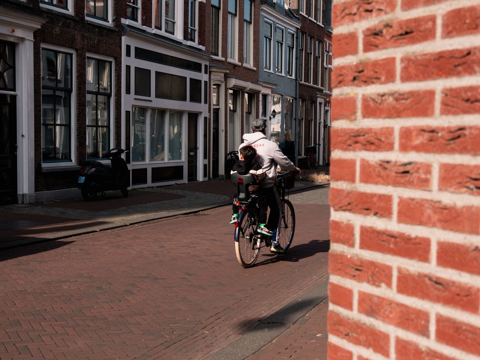 Een vader fietst door een Nederlandse binnenstad met zijn kind in een fietsstoeltje achterop