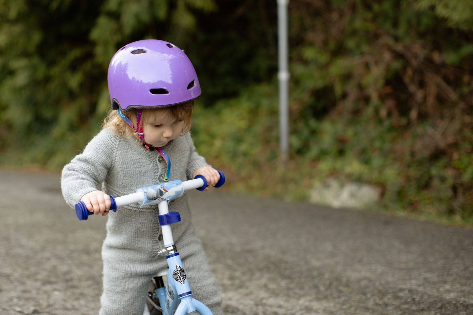 Een peuter met helm die geconcentreerd op een loopfiets rijdt