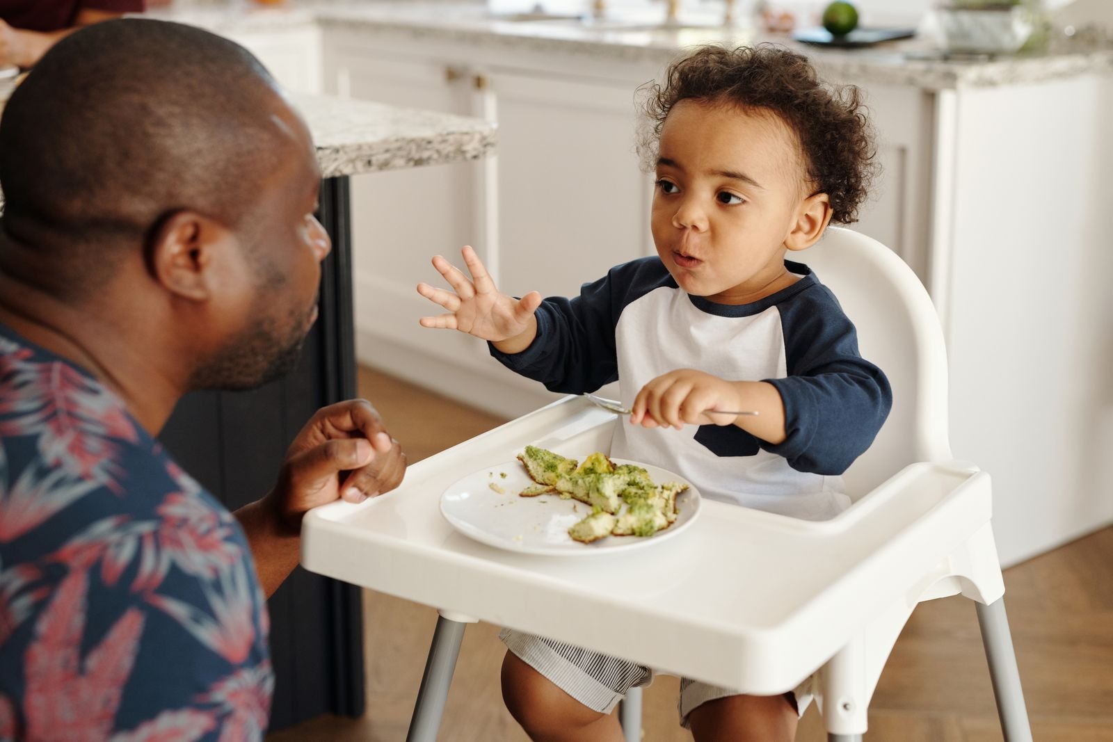 Vader die aandachtig naast zijn peuter aan de kinderstoel blijft terwijl die zelf met een vorkje eet