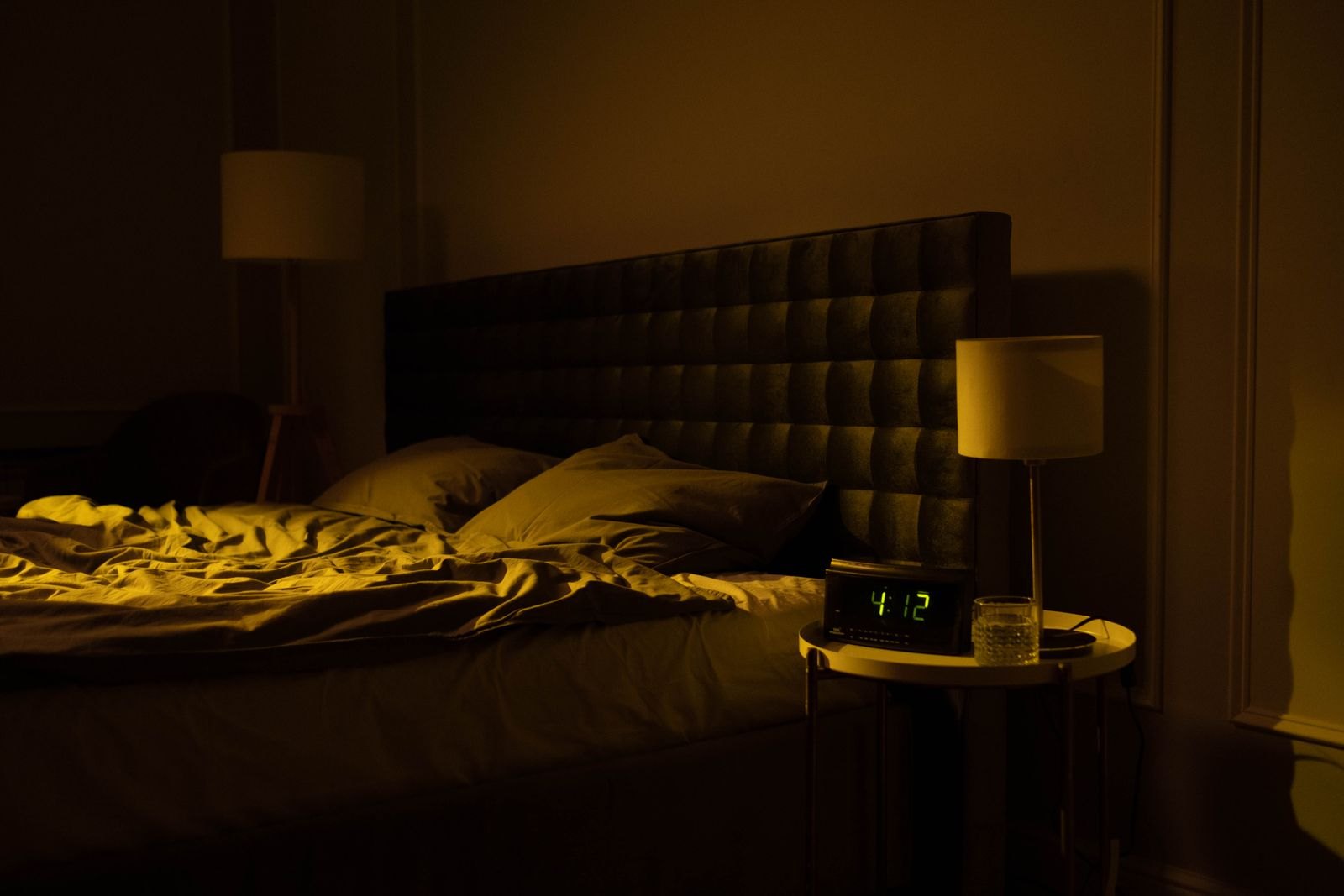 Een lege slaapkamer midden in de nacht, met een wekker die 4:12 uur aangeeft naast het bed