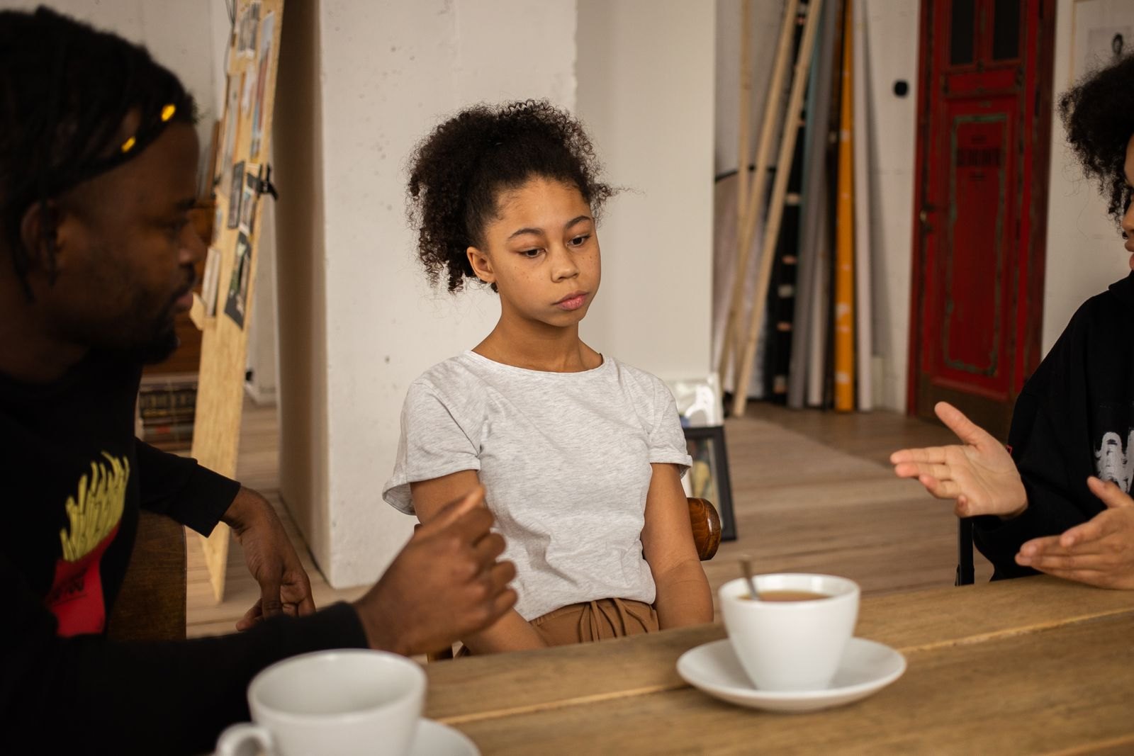 Een kind kijkt naar beneden terwijl twee volwassenen om haar heen gebaren tijdens een gesprek