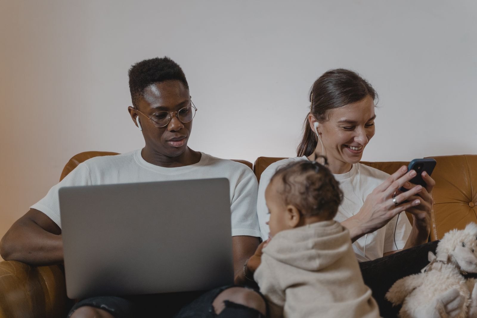 Een vader werkt geconcentreerd op zijn laptop terwijl de moeder naast hem met de baby op schoot tegelijk haar telefoon checkt