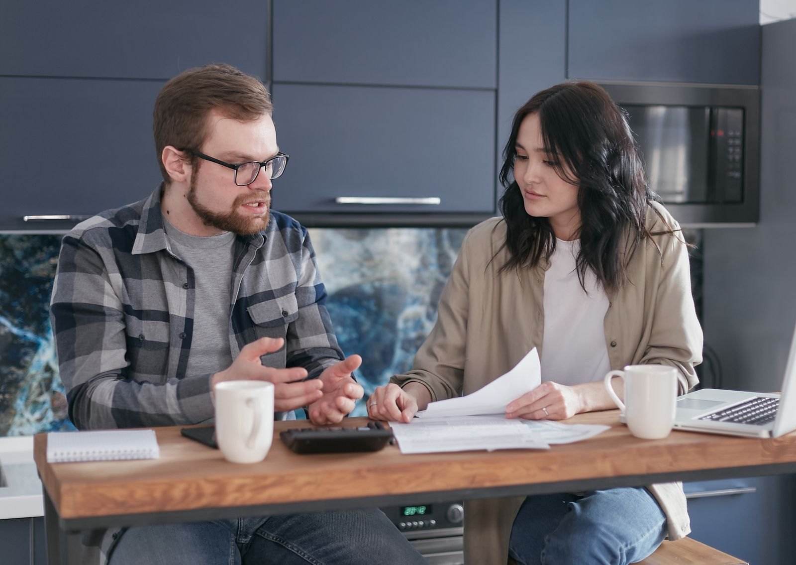 Een stel bespreekt samen de planning aan de keukentafel, met papieren en een laptop erbij