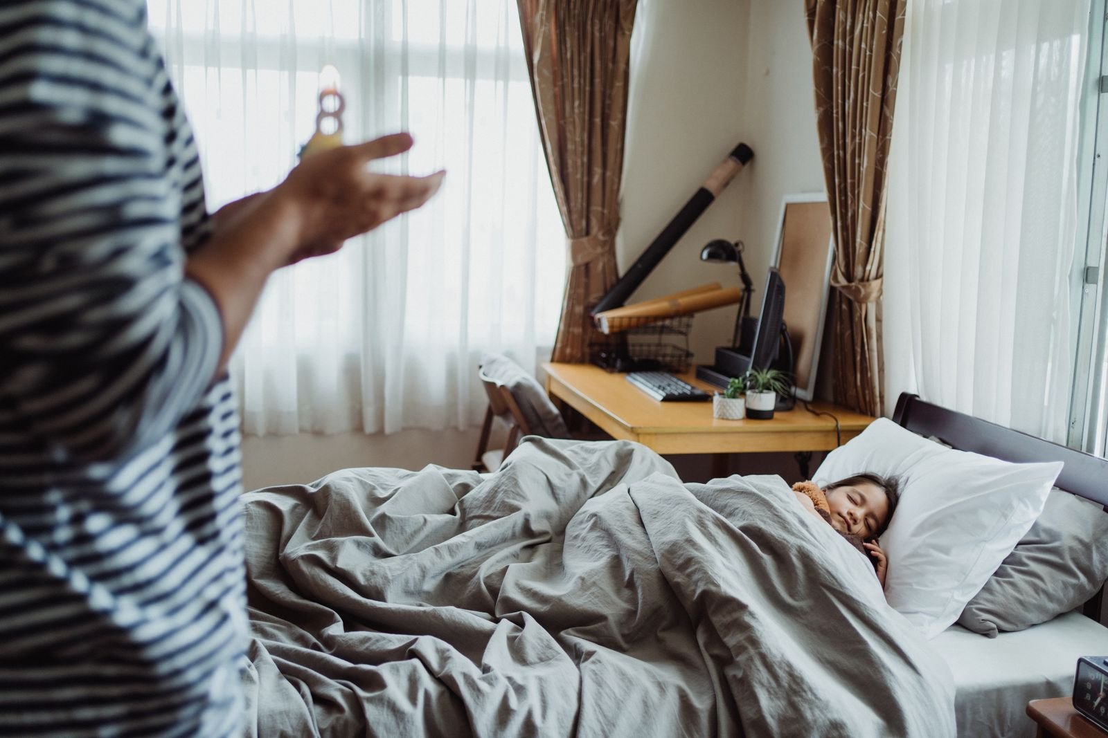 Een kind slaapt in bed terwijl er nog fel daglicht door de gordijnen naar binnen valt