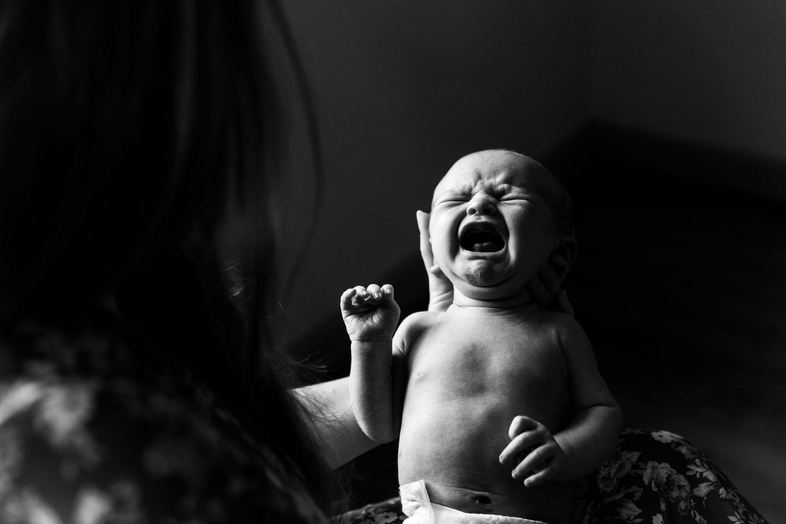 Zwart-witfoto van een huilende baby met gebalde vuistjes die getroost wordt door een ouder