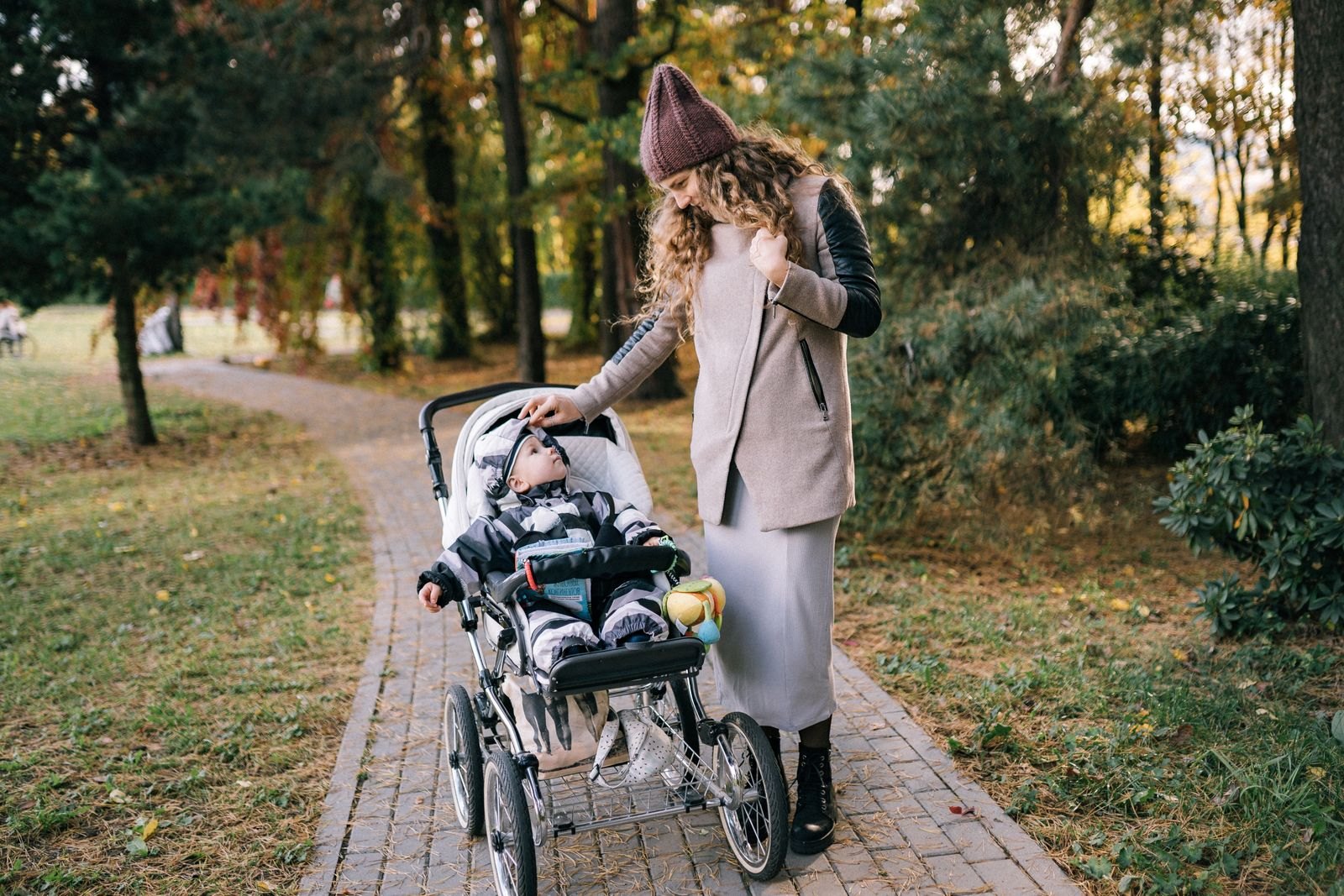 En förälder ler mot ett barn som sitter i en barnvagn i en park en solig höstdag
