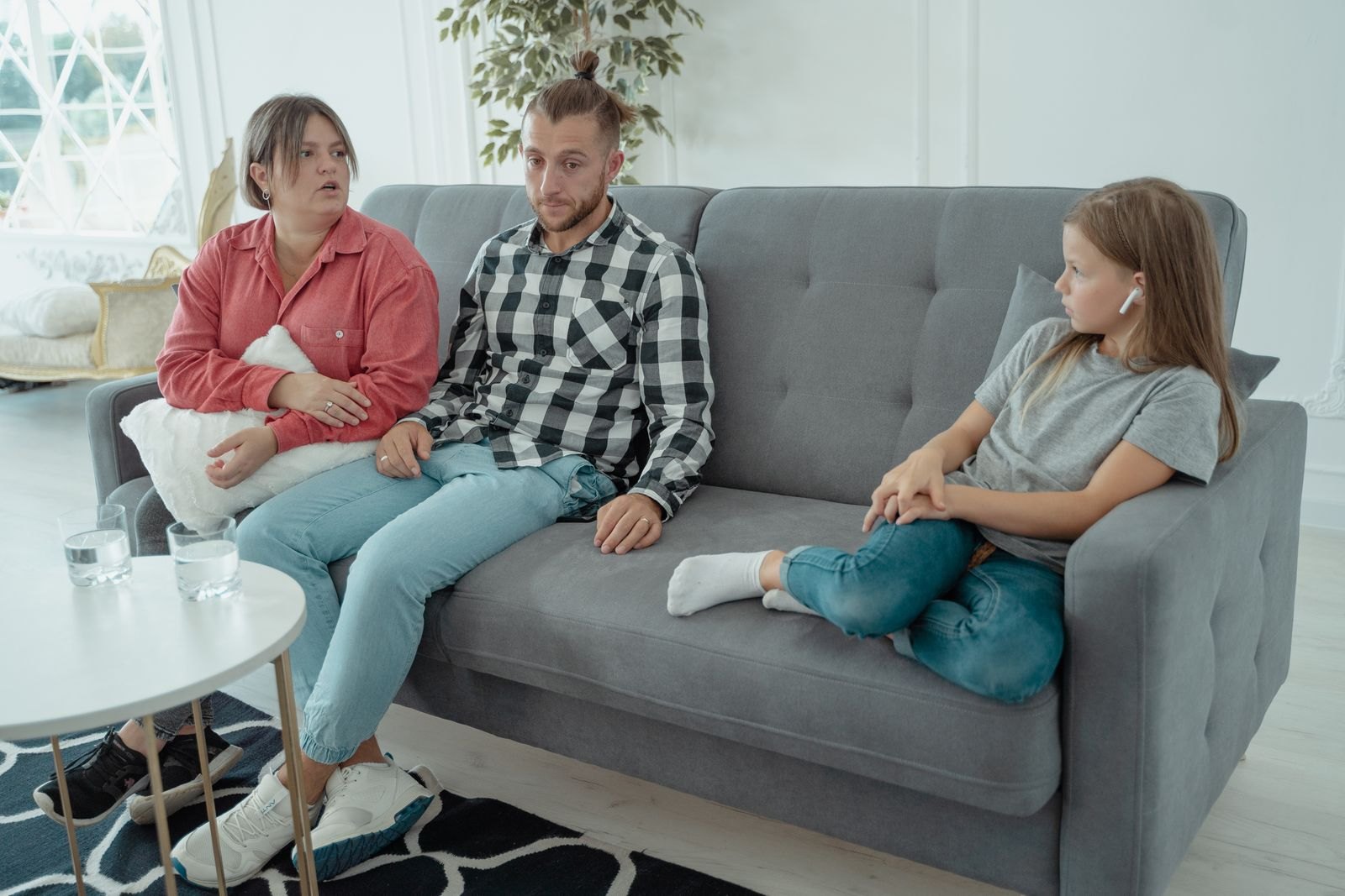 En familj sitter tyst i soffan, barnet har hörlurar i och tittar bort medan föräldrarna sitter blickstilla bredvid