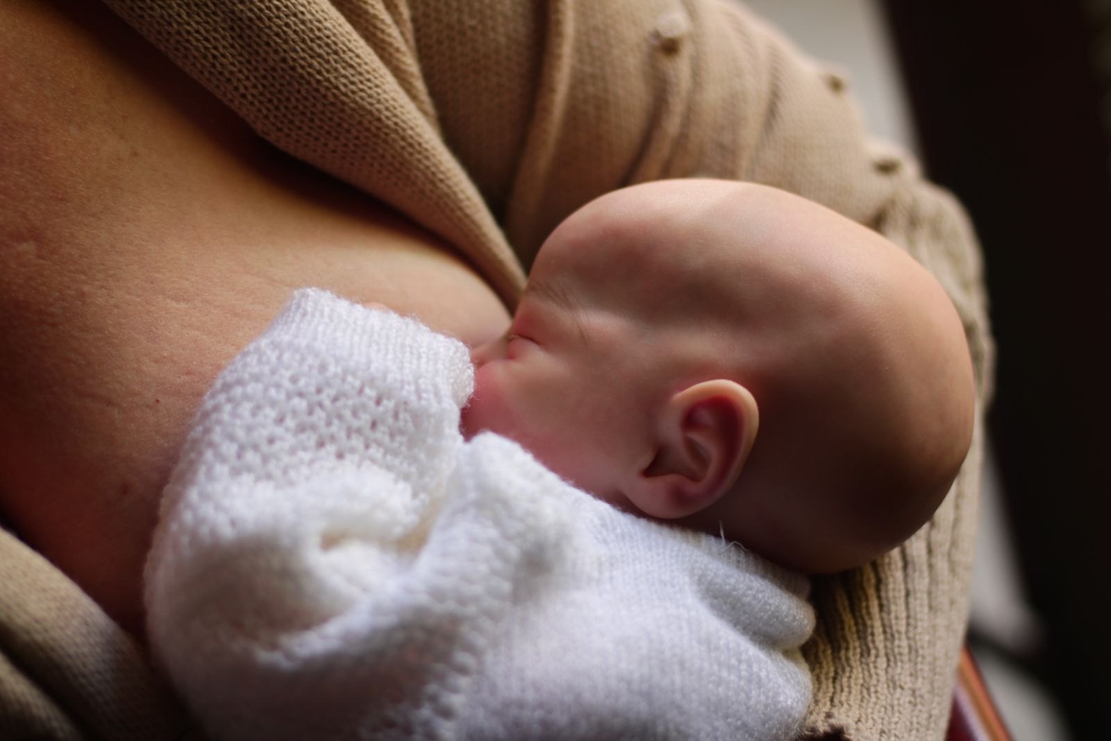 En nyfödd bebis ammar lugnt i mammas famn, varmt inomhusljus