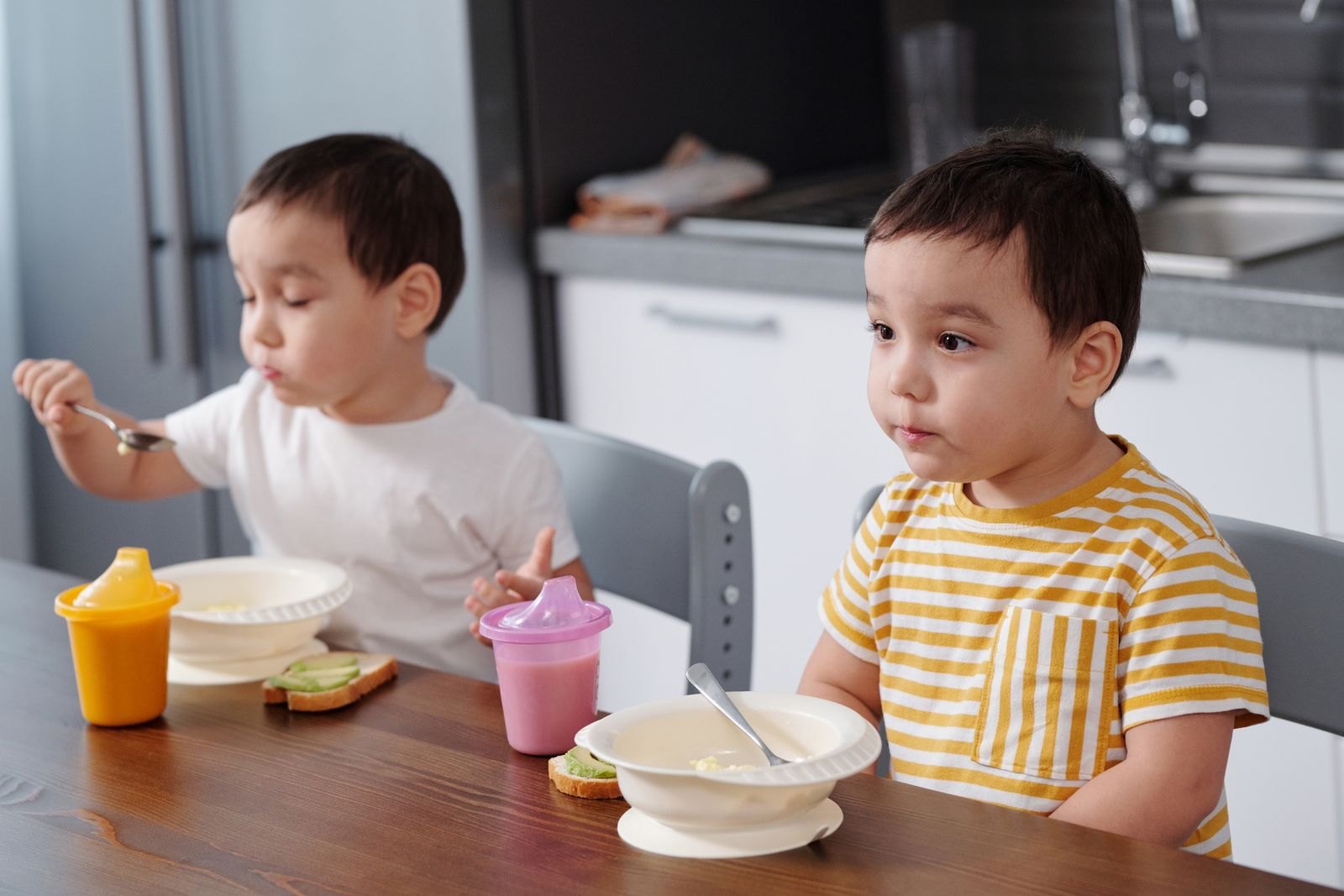 Småbarn äter frukost vid bordet med varsin pipmugg