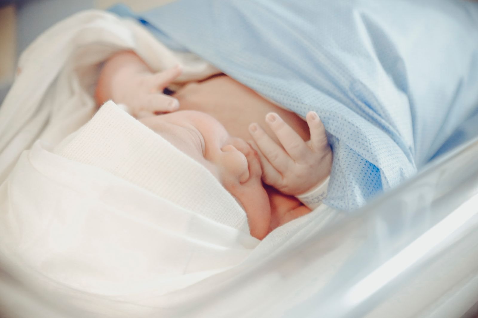 En nyfödd bebis lindad i sjukhusfilt med namnband runt handleden, precis efter förlossningen