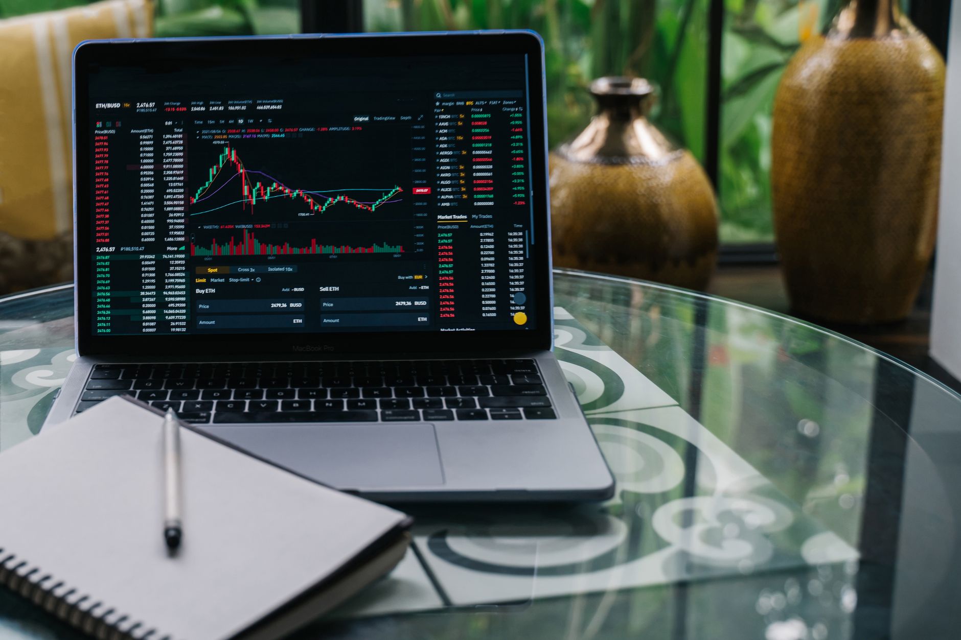 A laptop displaying a stock trading chart on a desk next to a notebook and pen