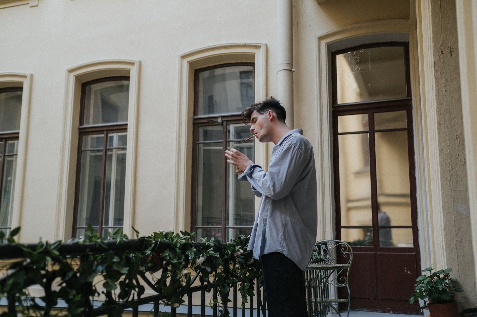 A person standing outdoors holding a lit cigarette with smoke drifting upward, illustrating how tobacco smoke raises collagen-cutting MMP-1 in skin