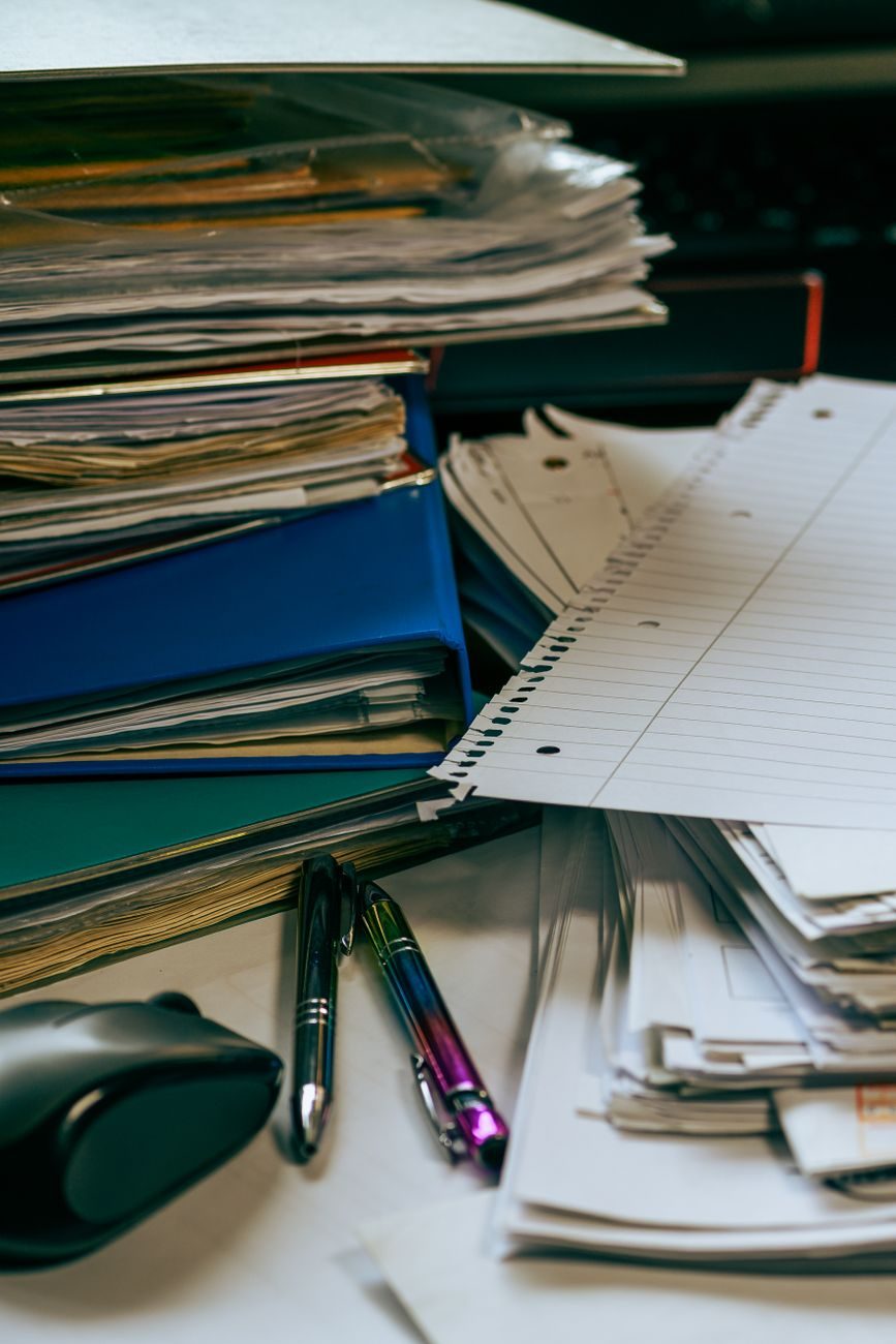 A stack of paperwork on a desk, standing in for the long uninterrupted sitting of an office day