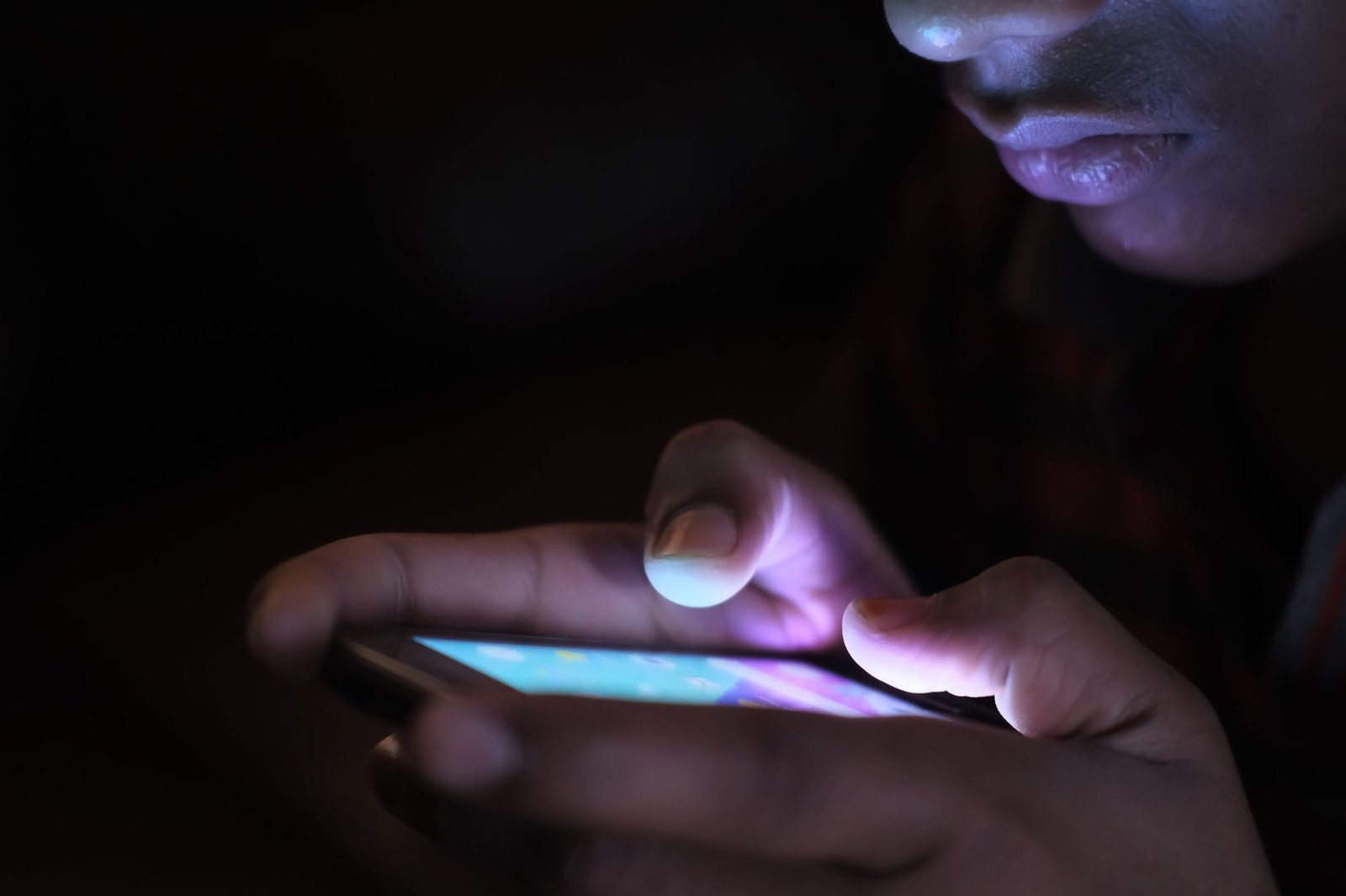 A smartphone glowing in a dark bedroom, a source of blue light that can suppress melatonin before sleep