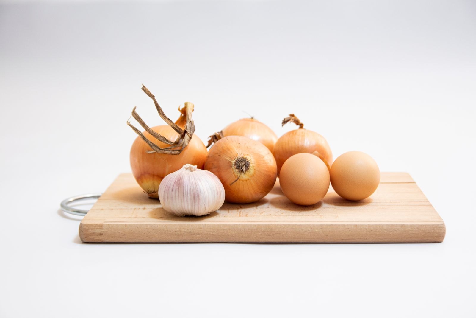 Zwiebeln, Knoblauch und Eier liegen nebeneinander auf einem Holzbrett