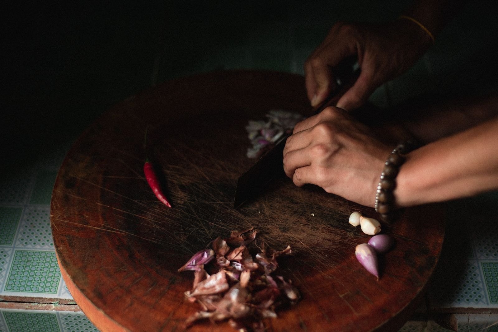 Manos picando chalotas y ajo sobre una tabla de madera, con un chile al lado