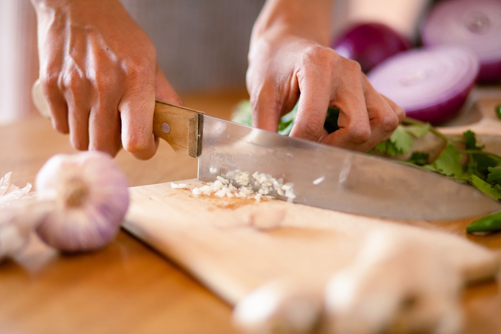 Handen snijden knoflook en rode ui fijn op een snijplank in de keuken
