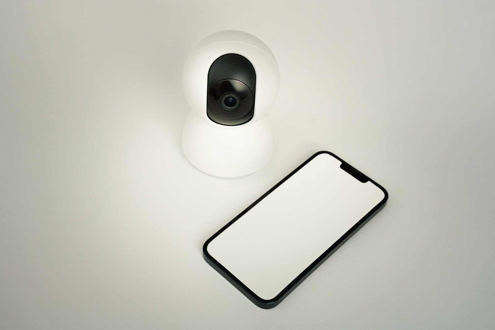 Telecamera di sorveglianza generica bianca accanto a uno smartphone con schermo vuoto, nessun marchio visibile