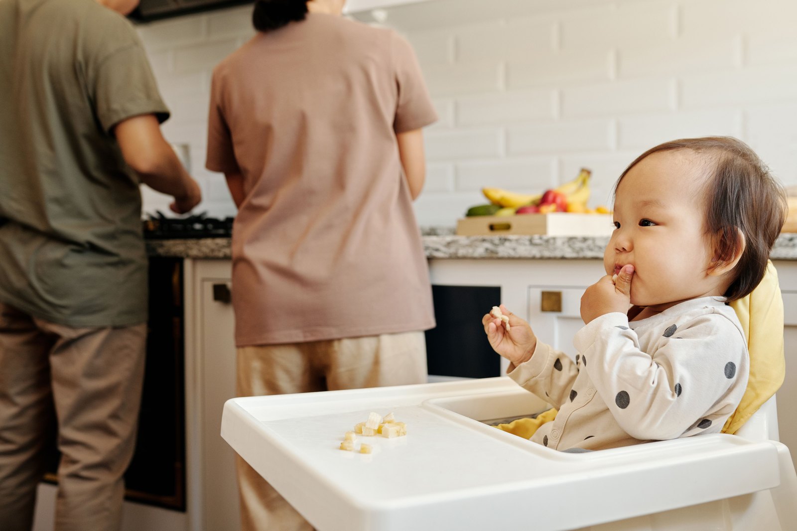ハイチェアに座り自分で果物をつまんで食べる乳幼児