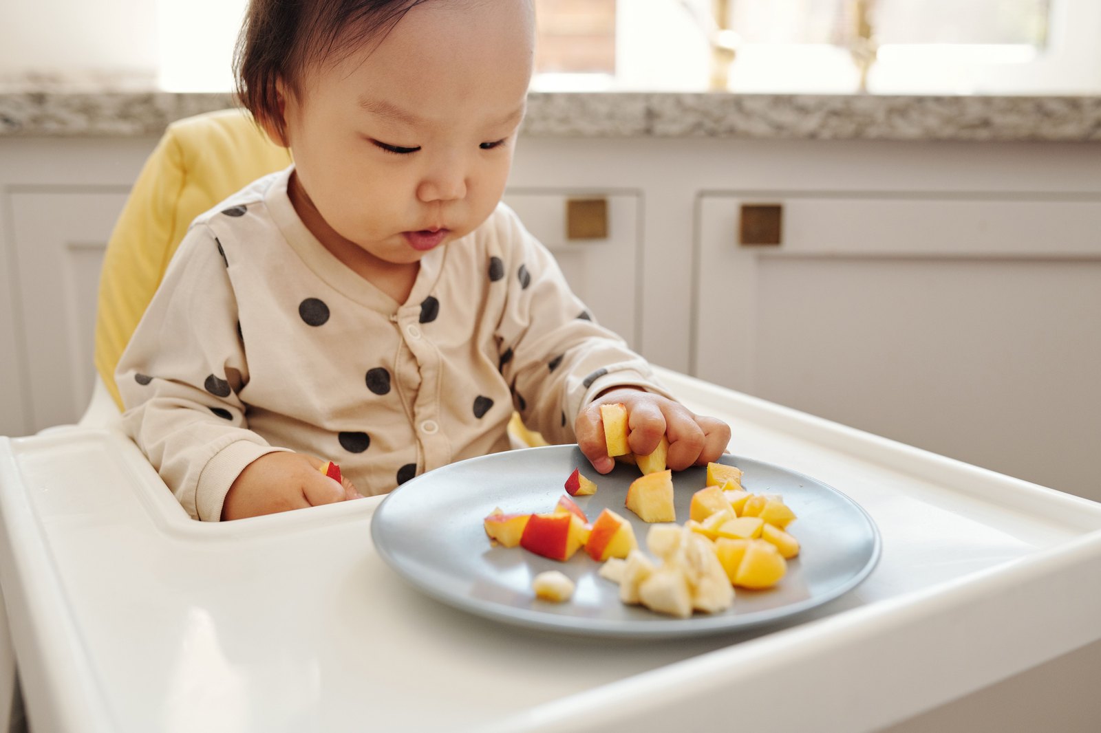 ハイチェアで果物の盛られた皿を見つめる赤ちゃん