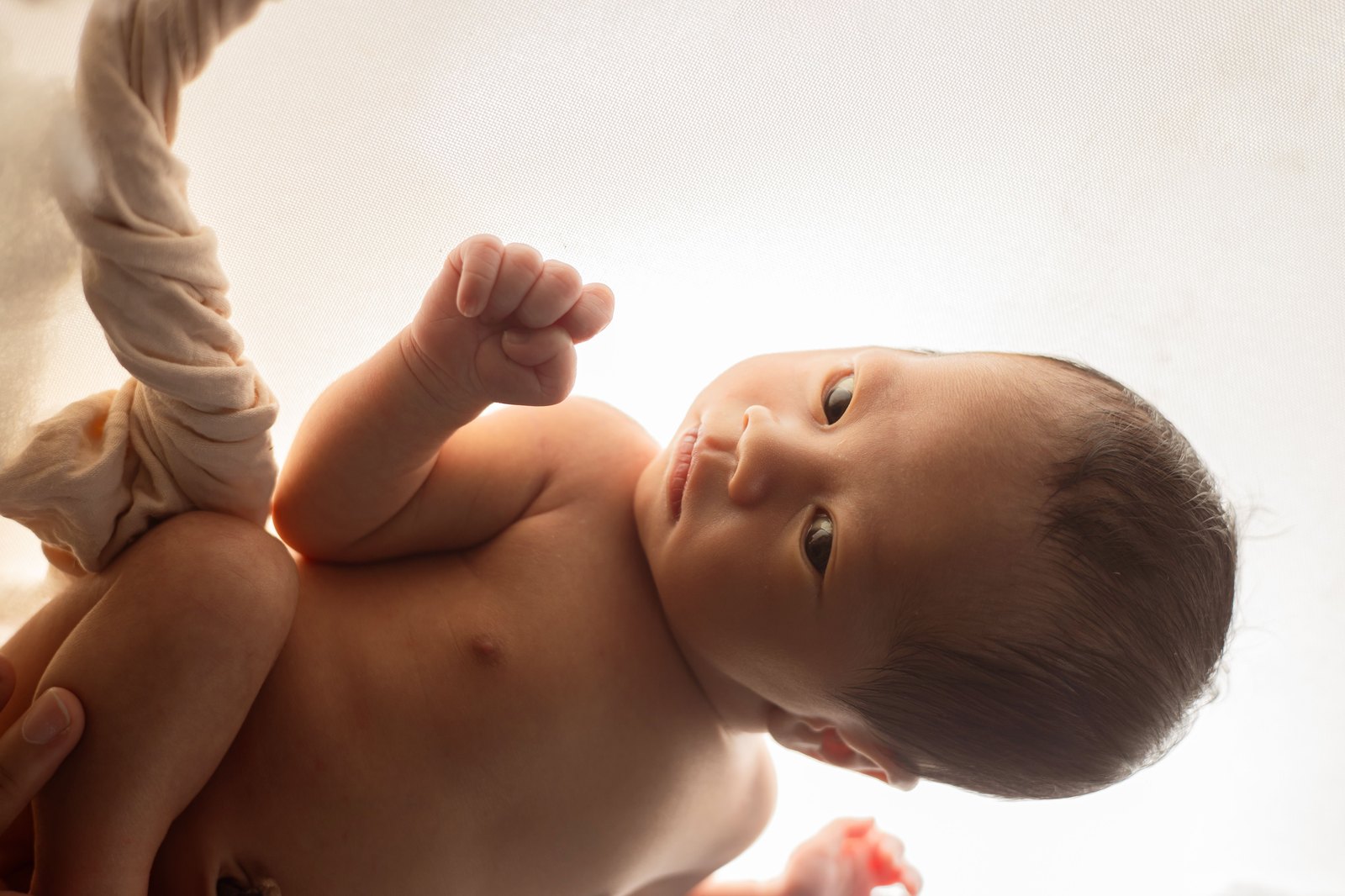 こぶしを握って持ち上げている新生児