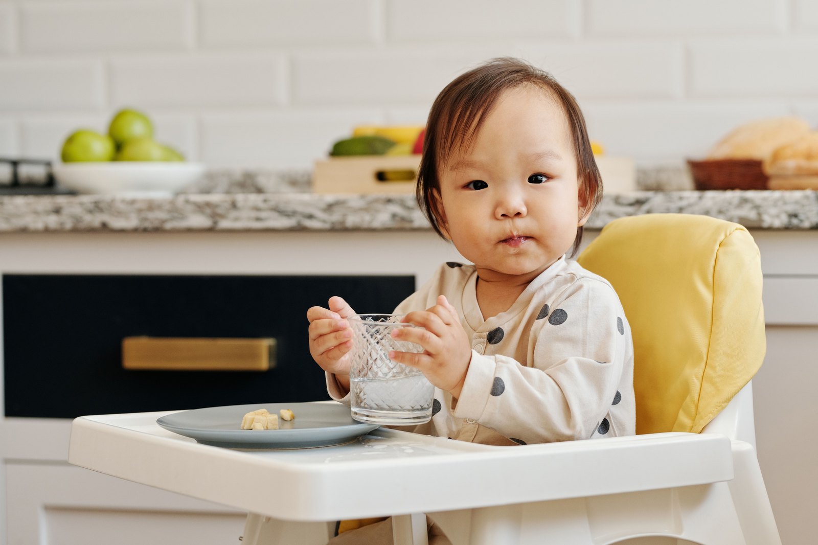 ハイチェアでコップを両手で持ち、自分で水を飲む赤ちゃん