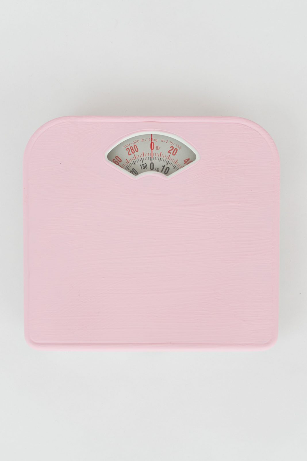 흰 바닥 위에 놓인 분홍색 아날로그 체중계를 위에서 내려다본 모습, 눈금은 0kg을 가리키고 있음