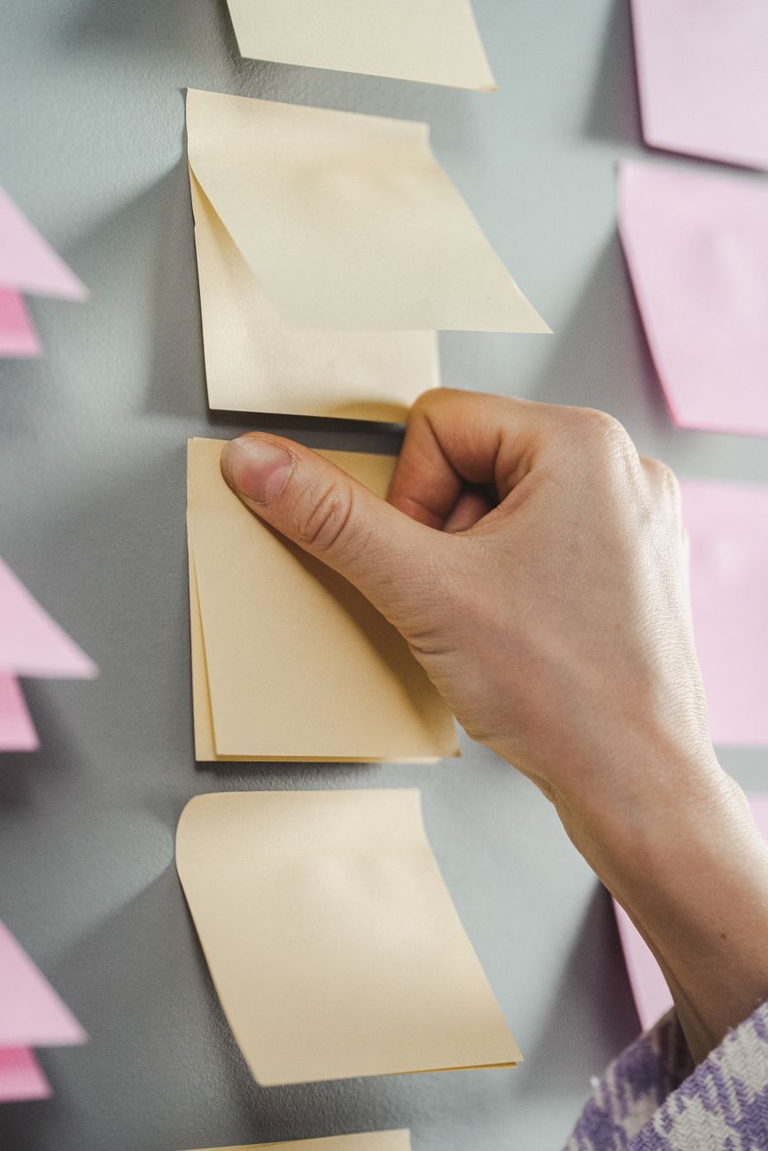Een hand die een van meerdere blanco memoblaadjes aan een muur kiest, als symbool voor het bepalen van een volgorde van schulden